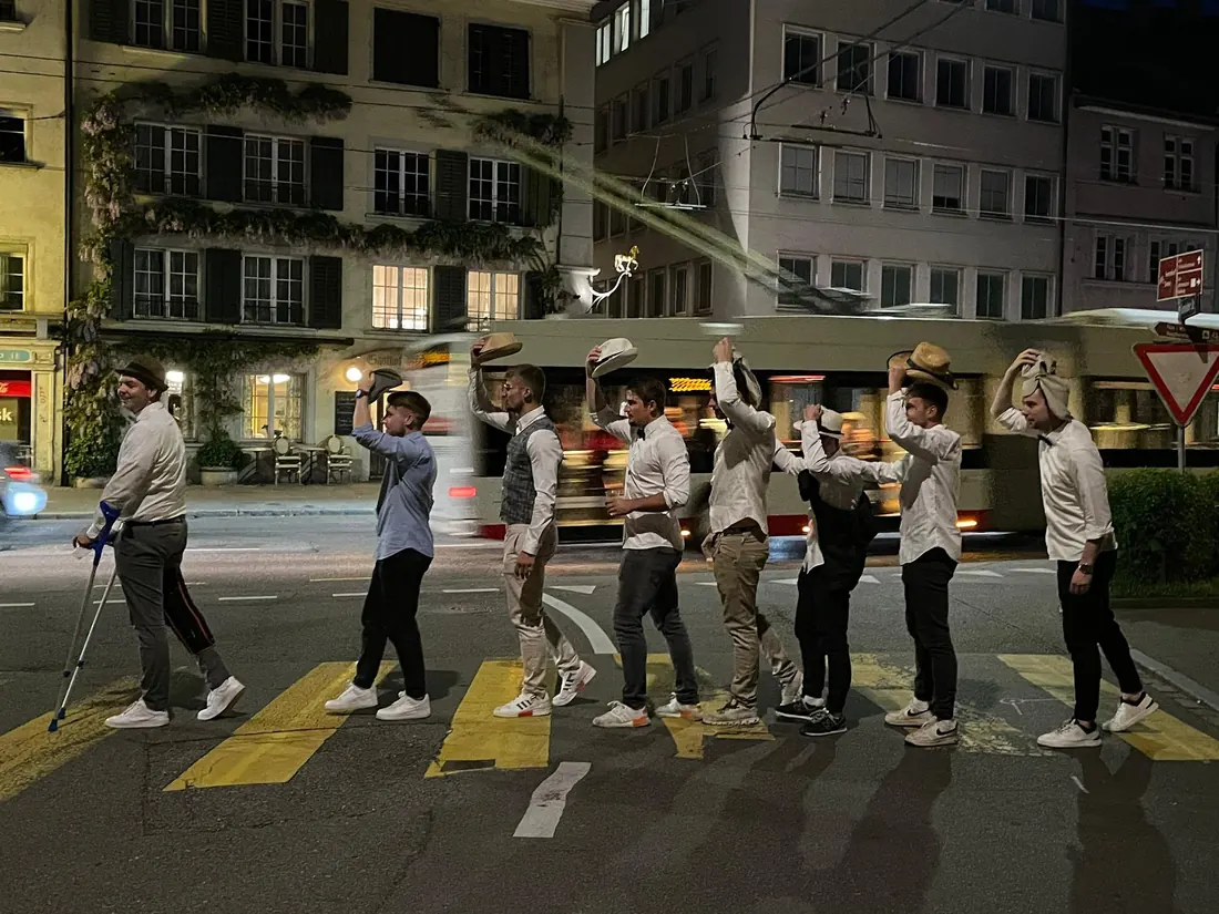 Eine Gruppe in weissen Hemden mit Hüten überquert nachts einen Fussgängerstreifen in Winterthur.